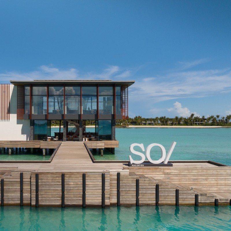 Luxurious waterfront resort in the Maldives featuring modern architecture and a wooden dock with "SO/ Maldives" signage.
