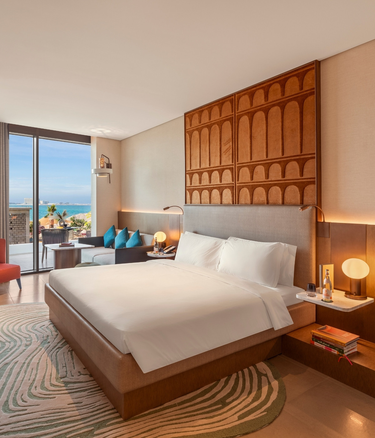 A modern hotel room featuring a king bed, elegant decor, a view of the ocean, and stylish seating area with vibrant accents.