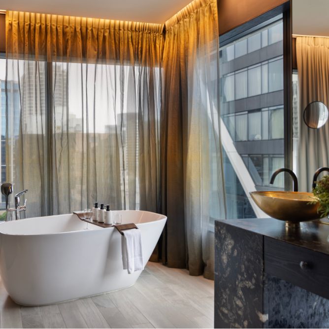 A stylish modern bathroom featuring a freestanding tub, elegant drapes, and a sleek sink with a view of the city skyline.
