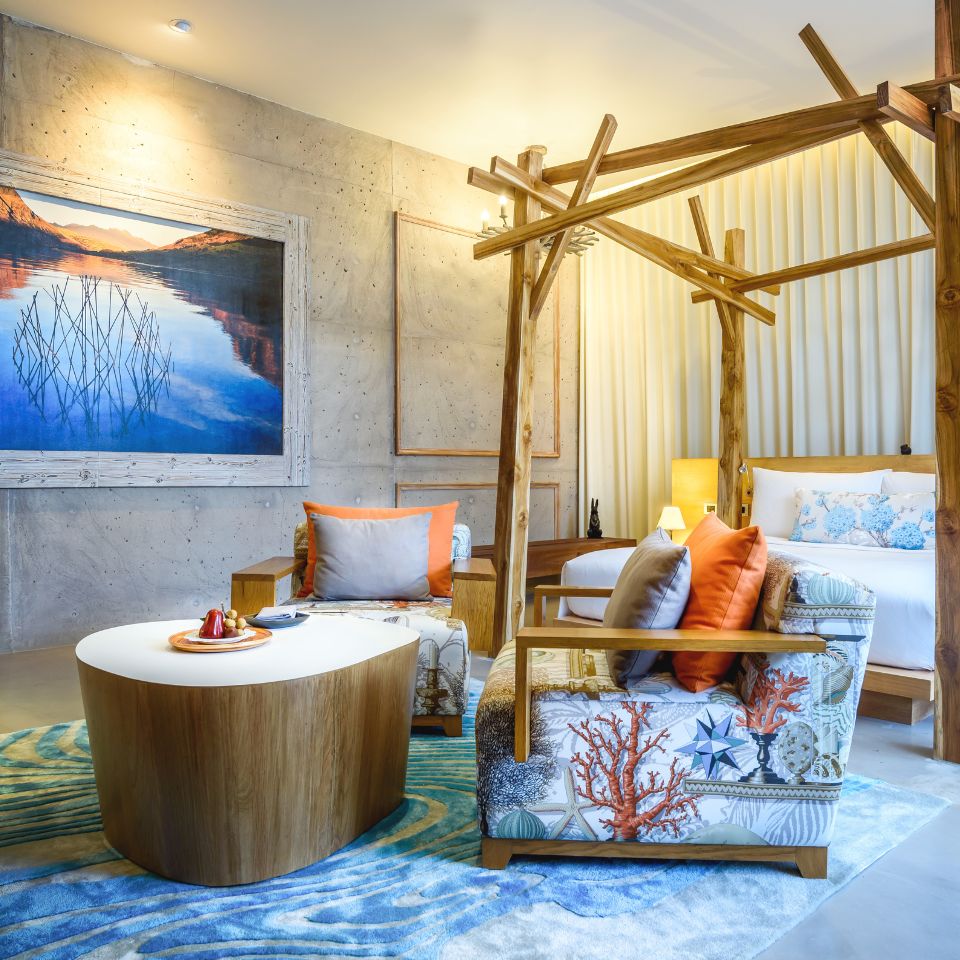 A cozy hotel room features a king-sized bed, vibrant cushions on a sofa, warm lighting, and nature-inspired decor, creating a serene ambiance.