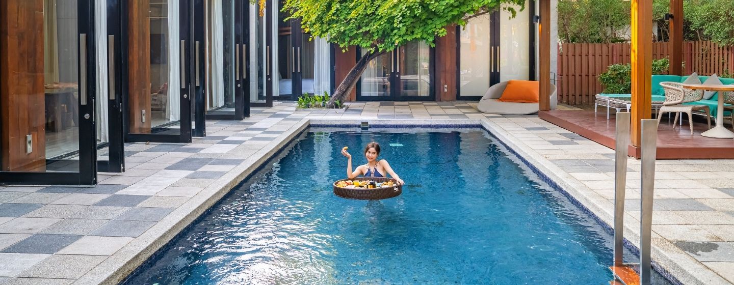 A wide view of a luxury private pool villa at SO/ Sofitel Hua Hin, featuring a guest enjoying a floating breakfast tray in the pool, surrounded by modern architecture and a private patio.