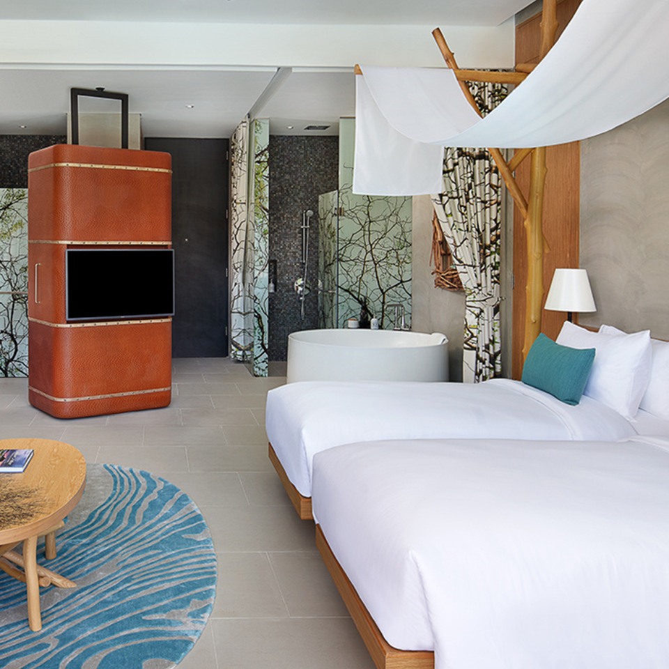 A cozy hotel room features a king-sized bed, vibrant cushions on a sofa, warm lighting, and nature-inspired decor, creating a serene ambiance.