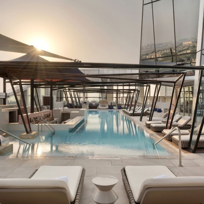 Sunset over a sleek rooftop infinity pool, surrounded by modern architecture and white loungers, creating a serene and luxurious ambiance.