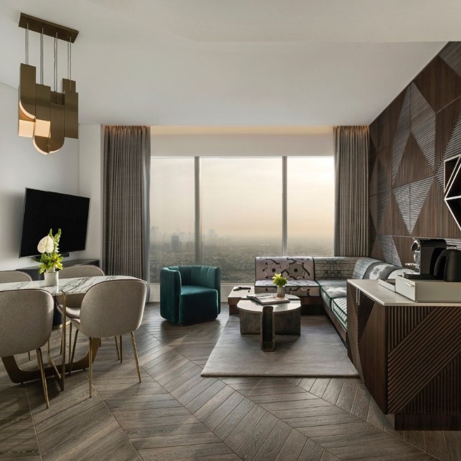 Luxurious modern hotel room with large windows offering a city view. Features a plush bed, stylish lamps, and cozy seating, creating a serene ambiance.