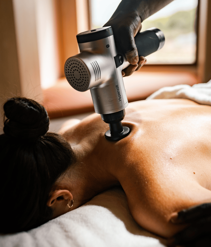 Una persona recibe un tratamiento muscular con una pistola de masaje HyperVolt centrada en la parte superior de la espalda, lo que mejora la relajación y la recuperación.
