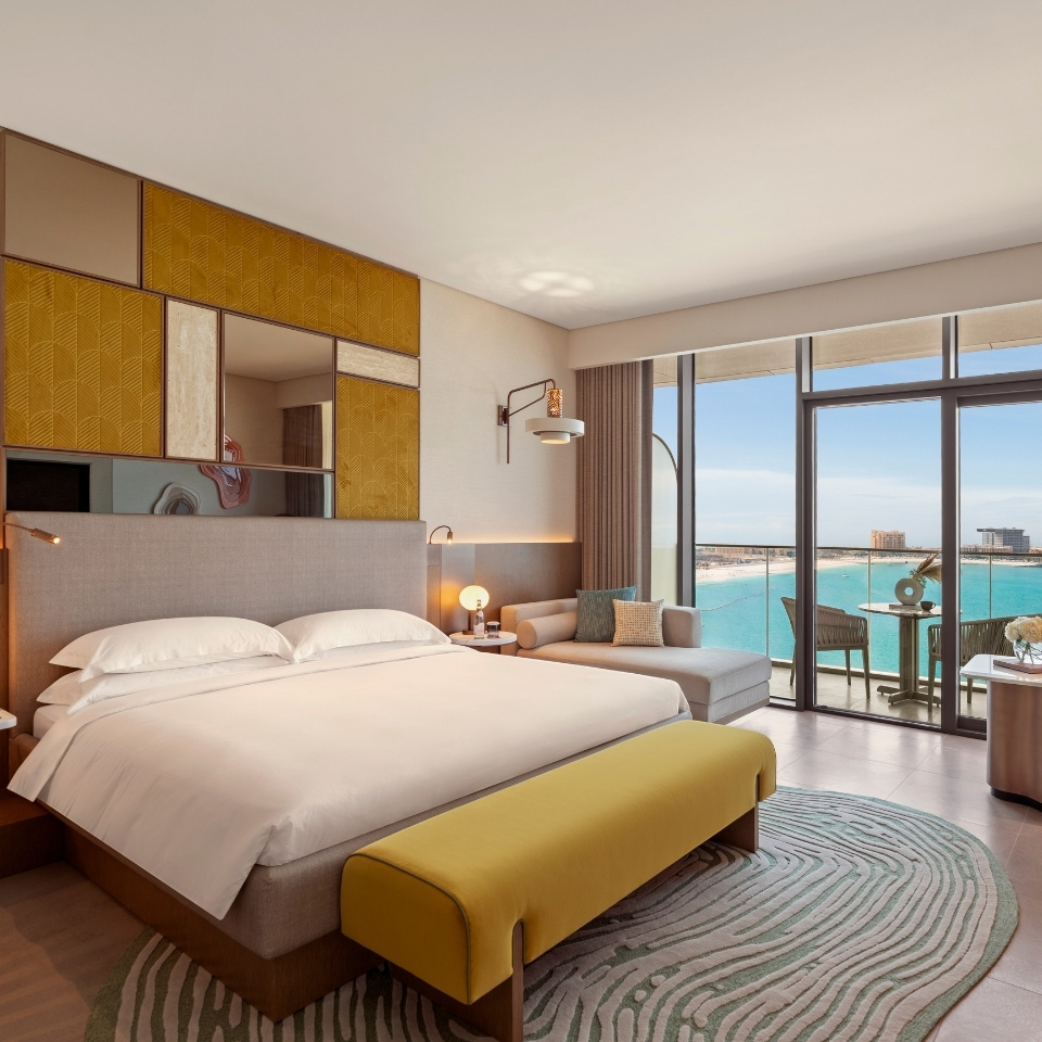 A stylish hotel room featuring a king bed, a cozy seating area, and large windows showcasing a beautiful ocean view.