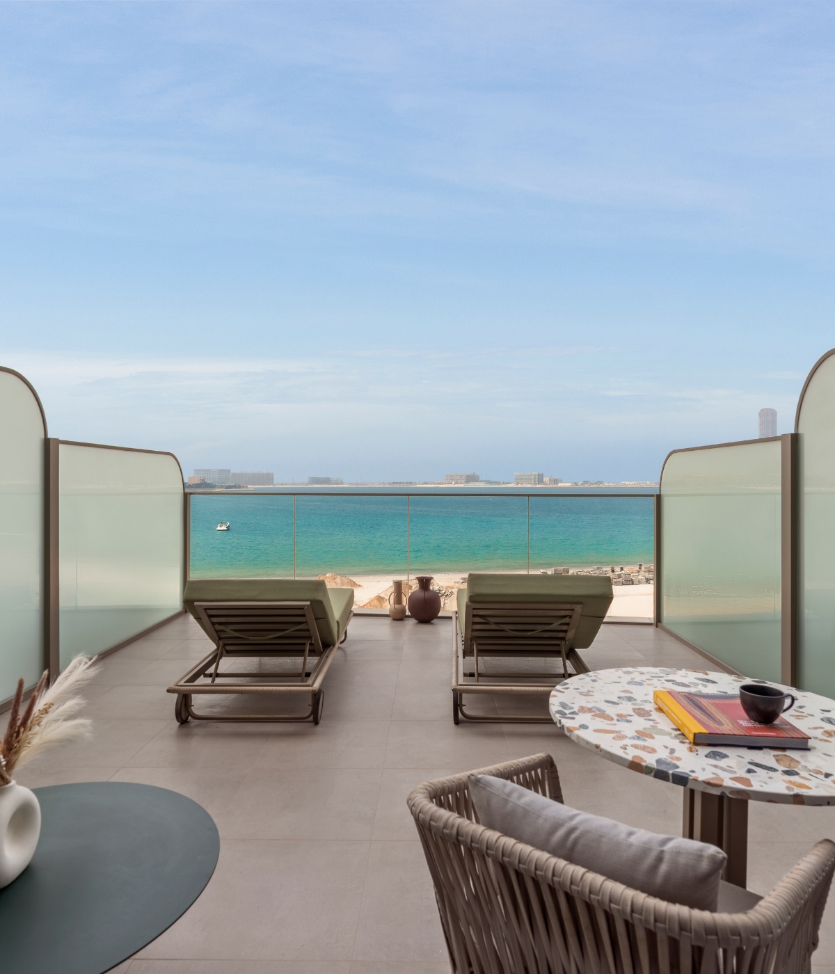 Serene balcony view with two lounge chairs facing a blue ocean under a clear sky. A cozy seating area with a small table and decor in the foreground.