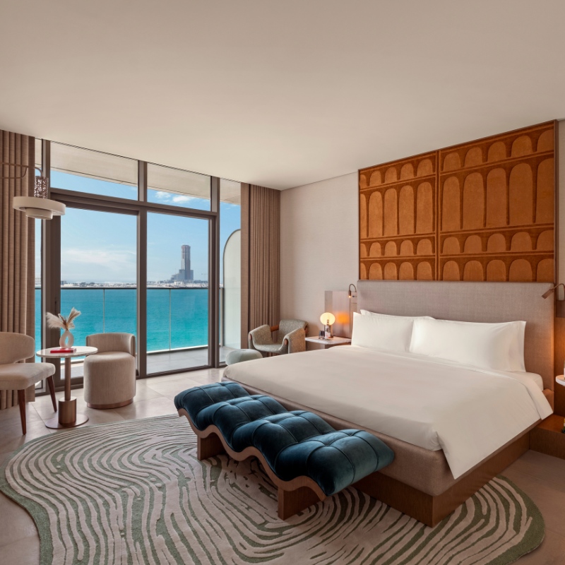 Luxurious hotel room with ocean view. Elegant design features a large bed, stylish furniture, and modern decor. Calm, inviting ambiance.