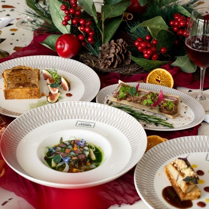Festive dining scene with elegant dishes on patterned plates, surrounded by pinecones, red berries, and orange slices, creating a luxurious, celebratory atmosphere.