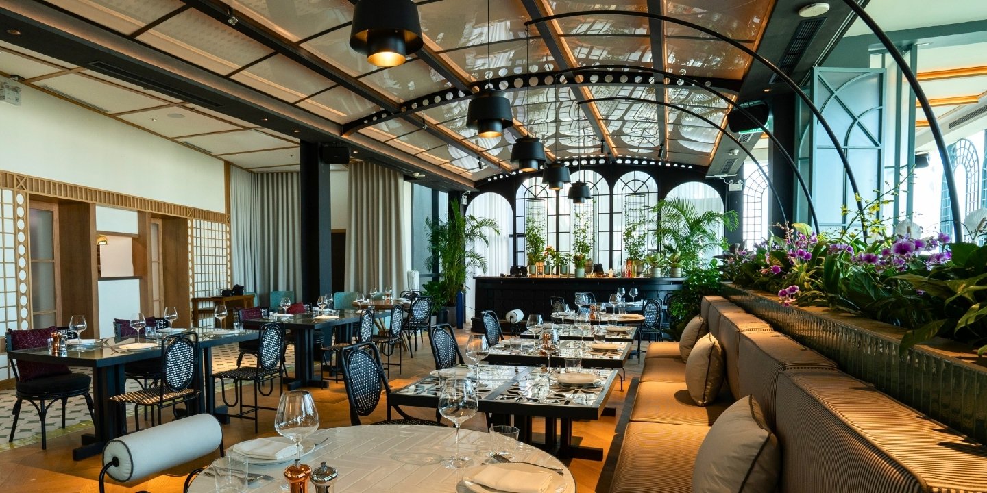 Elegant restaurant interior with stylish tables, plush seating, greenery, and decorative lighting, creating a warm, inviting atmosphere.