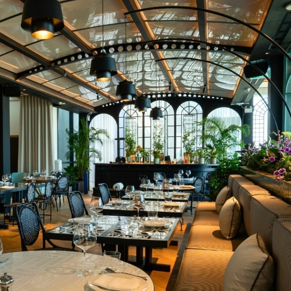 Elegant restaurant interior with stylish tables, plush seating, greenery, and decorative lighting, creating a warm, inviting atmosphere.