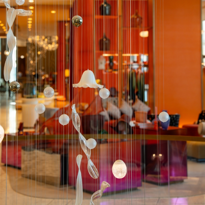 A decorative glass installation in a bright orange lobby, featuring various shaped glass pieces suspended from clear threads.