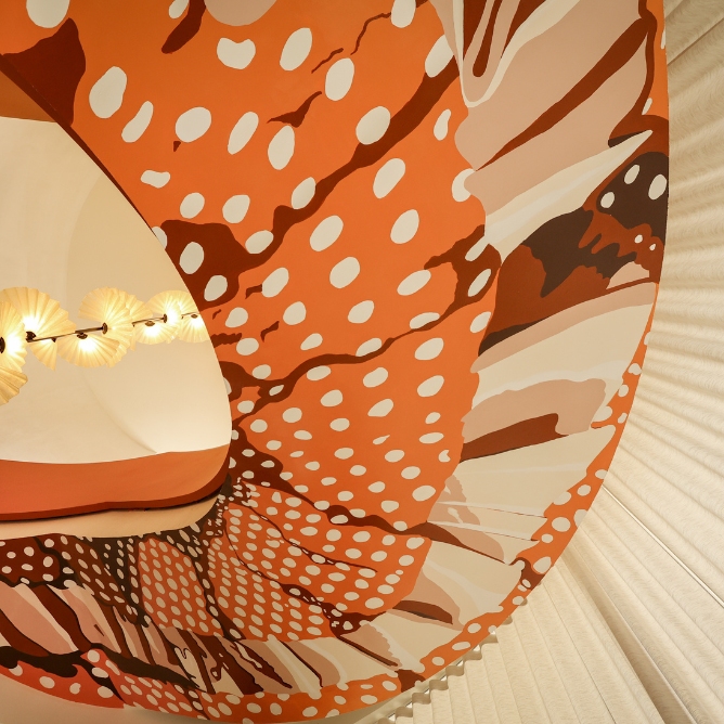 A vibrant, abstract ceiling mural in warm hues of red and orange, decorated with playful polka dots and organic shapes.