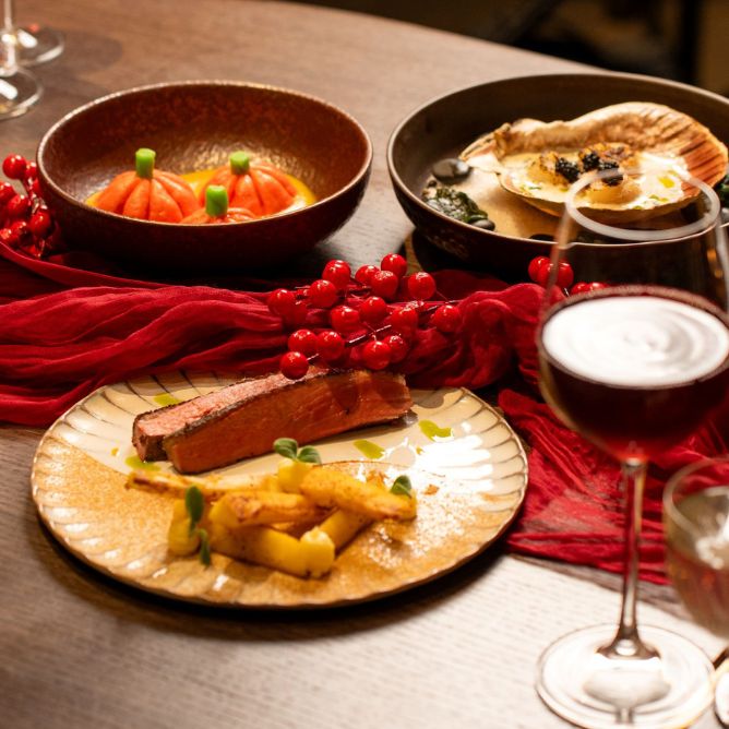 Elegant dinner setting with gourmet dishes arranged on a table. A salmon filet with potatoes, decorative pumpkins, and scallops with garnish.