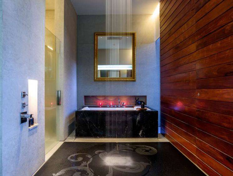 A luxurious spa bathroom featuring a large rain shower head above a black marble bathtub, warm mood lighting, and a golden framed mirror, creating a serene atmosphere.