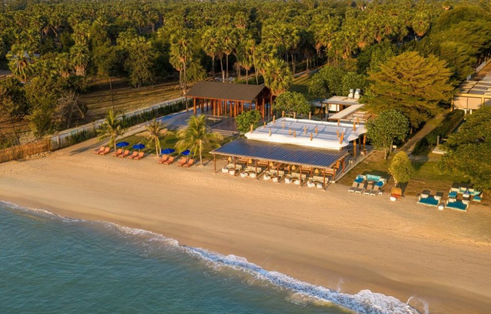 http://Stunning%20aerial%20view%20of%20a%20tropical%20sandy%20beach%20and%20turquoise%20ocean,%20adjacent%20to%20a%20beachfront%20resort%20with%20a%20large%20swimming%20pool,%20dining%20area,%20and%20dense%20palm%20grove.