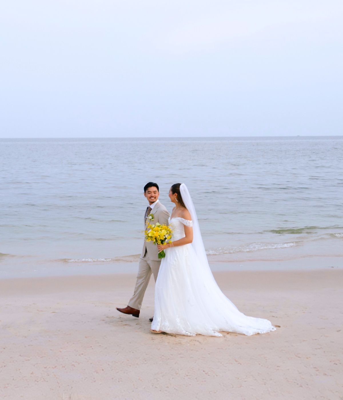 A couple joyfully walks hand in hand through a long beachfront at SO/ Sofitel Hua Hin