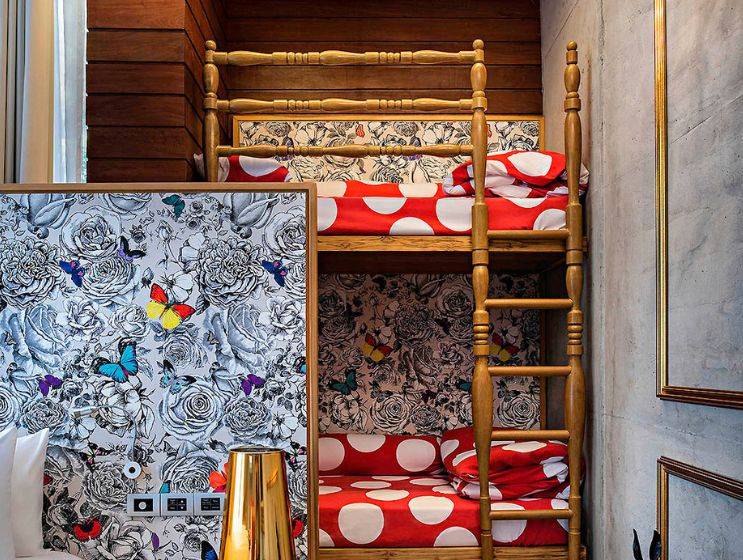A fun, wood-paneled kids' room featuring a wooden bunk bed with orange polka-dot bedding, a blue beanbag chair where a boy reads, and a girl sitting on the top bunk.