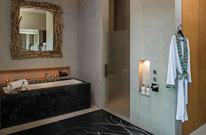 http://A%20luxurious%20modern%20spa%20bathroom%20featuring%20a%20deep%20soaking%20tub%20clad%20in%20dark%20marble,%20a%20glass%20walk-in%20shower,%20a%20branch-framed%20mirror,%20and%20a%20hanging%20white%20bathrobe%20with%20custom%20patterned%20trim.
