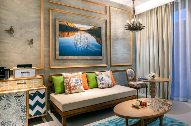 http://A%20chic%20hotel%20suite%20living%20area%20with%20a%20comfortable%20daybed,%20vibrant%20cushions,%20and%20a%20large%20framed%20artwork%20depicting%20a%20serene%20pond%20reflection,%20creating%20a%20tranquil%20atmosphere.