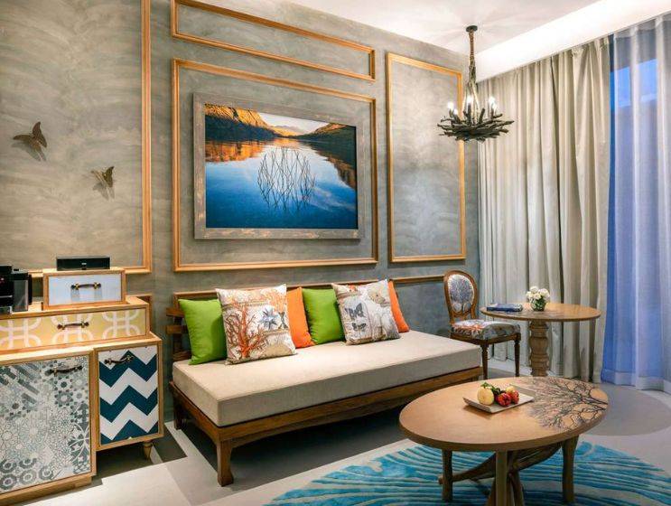 A chic hotel suite living area with a comfortable daybed, vibrant cushions, and a large framed artwork depicting a serene pond reflection, creating a tranquil atmosphere.