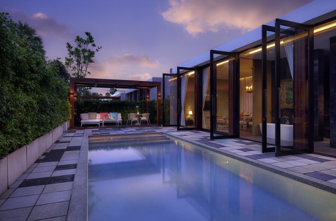 http://An%20inviting%20luxury%20private%20pool%20villa%20at%20dusk,%20with%20warmly%20lit%20interior%20rooms%20opening%20onto%20a%20tranquil%20swimming%20pool%20and%20a%20paved%20patio%20area,%20surrounded%20by%20lush%20trees.