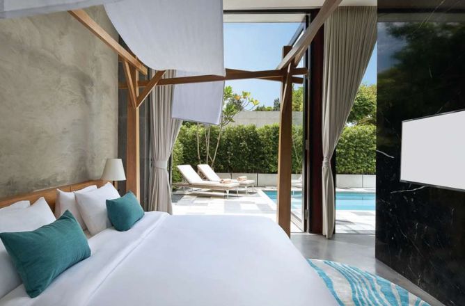 http://A%20bright%20hotel%20bedroom%20with%20white%20bedding%20and%20a%20wooden%20canopy%20bed%20frame,%20featuring%20large%20glass%20doors%20that%20open%20directly%20onto%20a%20private%20pool%20area%20with%20outdoor%20seating.