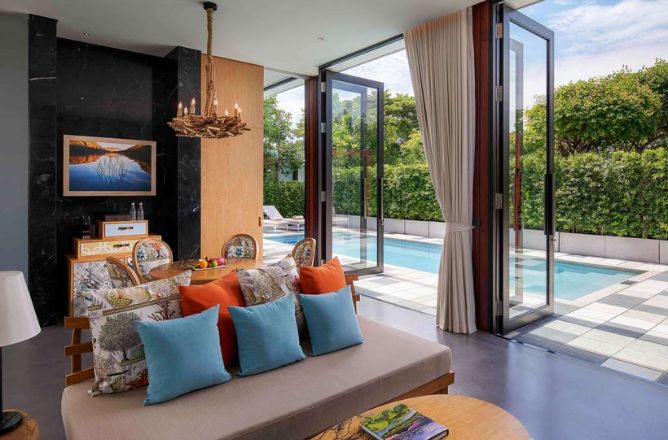 http://An%20elegant%20suite%20living%20area%20with%20a%20comfortable%20daybed,%20decorative%20cushions,%20and%20large%20folding%20glass%20doors%20that%20open%20wide%20to%20reveal%20a%20private%20swimming%20pool%20surrounded%20by%20greenery.