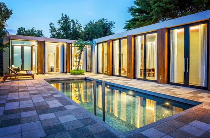 http://A%20modern%20luxury%20private%20pool%20villa%20at%20dusk,%20with%20warmly%20lit%20rooms%20opening%20onto%20a%20tranquil%20swimming%20pool%20and%20a%20paved%20patio%20area,%20surrounded%20by%20lush%20trees.