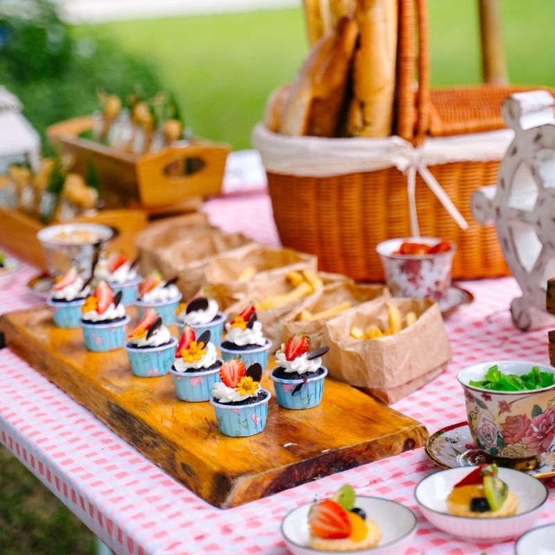 Outdoor picnic-style catering setup with cupcakes and snacks on a checkered tablecloth for private parties at SO/ Sofitel Hua Hin