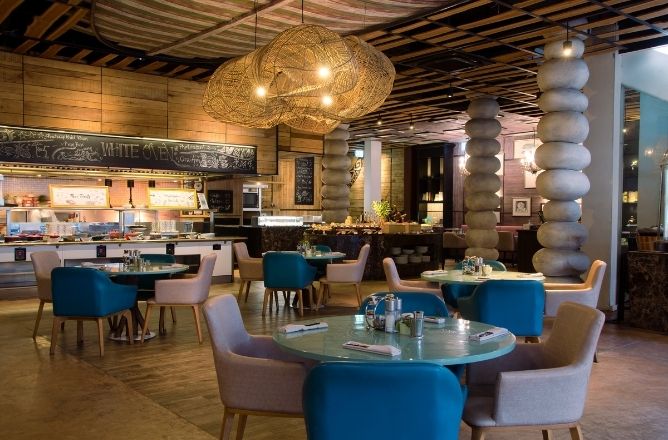 http://Stylish%20restaurant%20interior%20with%20colorful%20chairs%20and%20round%20tables%20under%20woven%20light%20fixtures.%20Wooden%20accents%20create%20a%20cozy,%20modern%20atmosphere.