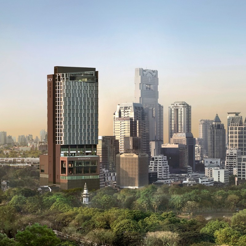 A modern skyscraper, with a sleek design and glass facade, stands prominently among other tall buildings in a city skyline, above a lush green park.