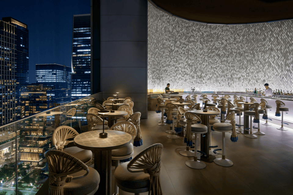 http://Wild%20Iris%20rooftop%20bar%20with%20curved%20marble%20counter,%20woven%20seating%20and%20glowing%20wall%20design%20overlooking%20Lumphini%20Park%20and%20the%20Bangkok%20skyline%20at%20night.