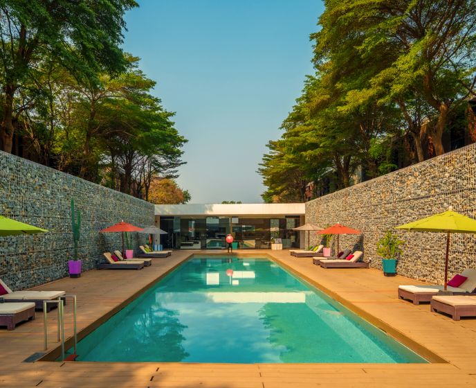 Luxurious resort pool scene with vibrant umbrellas and lounge chairs, surrounded by lush green trees, creating a serene and inviting atmosphere.