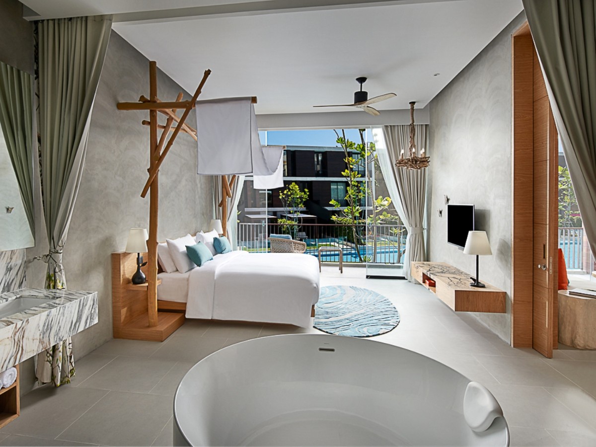 Modern luxury hotel room with a white bed, wooden accents, and marble sink. Open layout with a bathtub, balcony view, and pool visible outside. Calm and serene ambiance.