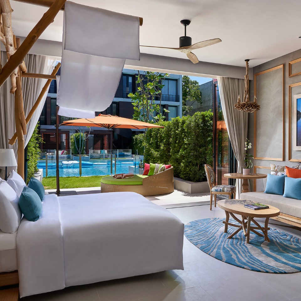 Luxurious hotel room with a pool view. Features a cozy bed, stylish sofa with colorful cushions, and modern decor with a serene, airy ambiance.