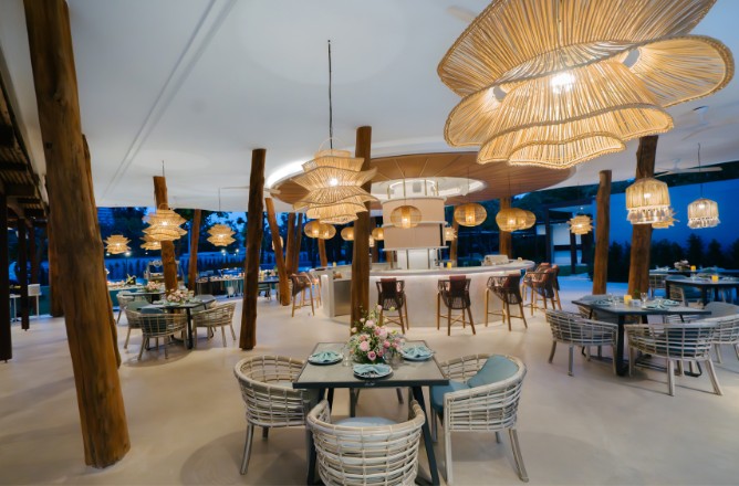http://Chic%20restaurant%20with%20rattan%20light%20fixtures,%20wicker%20chairs,%20and%20elegantly%20set%20tables.%20Wooden%20pillars%20add%20warmth,%20creating%20a%20cozy,%20inviting%20ambiance.