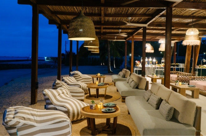 http://Beachside%20lounge%20with%20cozy%20sofas%20and%20striped%20chairs%20under%20woven%20pendant%20lights%20at%20night.%20Tables%20set%20with%20plates%20create%20a%20relaxed,%20inviting%20atmosphere.