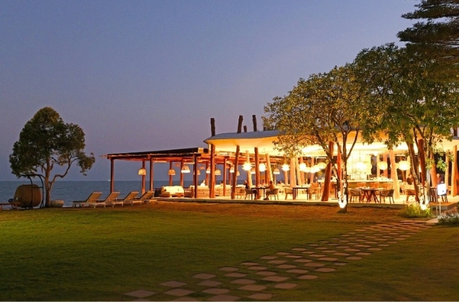 http://Outdoor%20beachside%20restaurant%20at%20dusk%20with%20warm%20lighting.%20Pathway%20leads%20through%20a%20lush%20green%20lawn%20to%20the%20open,%20inviting%20dining%20area.%20Peaceful%20and%20elegant.