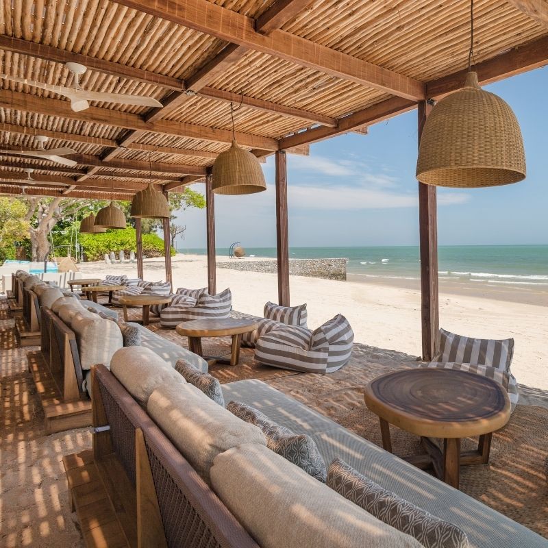 Beachfront dining setup with lounge seating and food under a shaded canopy at Beach Society, SO/ Sofitel Hua Hin
