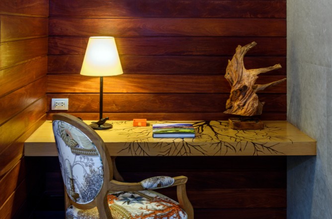 http://Cozy%20study%20nook%20with%20warm%20lighting.%20A%20wooden%20desk%20features%20a%20tree%20design,%20adorned%20with%20a%20driftwood%20sculpture%20and%20books.%20A%20patterned%20chair%20adds%20elegance.