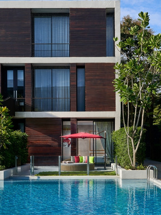 http://Modern%20three-story%20building%20with%20wooden%20facade,%20large%20windows,%20and%20a%20serene%20pool.%20A%20red%20umbrella%20and%20greenery%20add%20vibrancy%20and%20a%20relaxing%20tone.