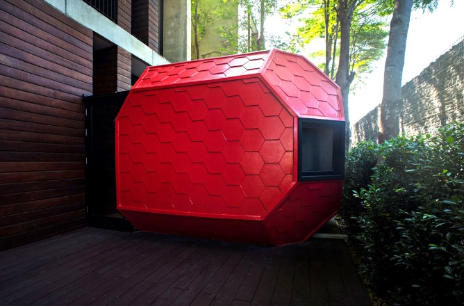 http://Red%20hexagonal%20pod%20with%20a%20window,%20attached%20to%20a%20modern%20building%20with%20wooden%20walls.%20Surrounded%20by%20greenery%20and%20trees,%20it%20creates%20a%20futuristic,%20cozy%20vibe.