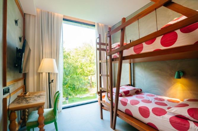 http://Cozy%20room%20with%20a%20wooden%20bunk%20bed%20featuring%20red%20polka%20dot%20bedding,%20a%20window%20with%20lush%20green%20trees%20outside,%20a%20wooden%20desk%20with%20a%20lamp,%20and%20a%20wall-mounted%20TV.