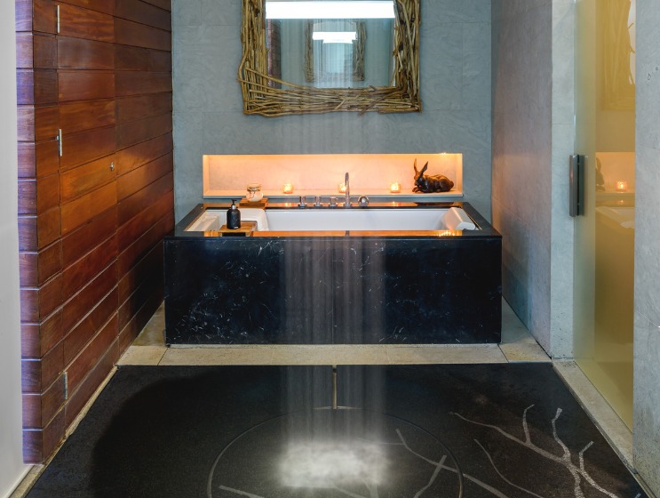 Modern bathroom with a sleek rainfall shower, black tub, and wood panel wall. A rustic mirror and soft lighting add warmth and elegance.