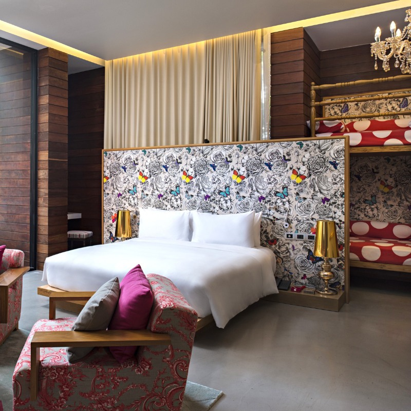 http://Stylish%20hotel%20room%20with%20a%20large%20bed,%20floral%20and%20butterfly-patterned%20headboard,%20and%20bold%20red%20polka%20dot%20bunk%20beds.%20Warm%20wood%20tones%20and%20gold%20accents.