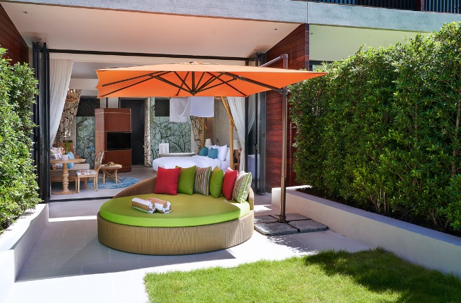 http://Spacious%20patio%20with%20a%20circular%20daybed,%20vibrant%20green%20and%20red%20cushions%20beneath%20an%20orange%20umbrella.%20Beyond,%20a%20cozy%20room%20opens%20with%20gentle,%20earthy%20tones.