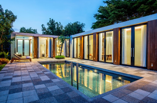 http://Modern%20poolside%20view%20of%20a%20contemporary%20house%20at%20dusk.%20Floor-to-ceiling%20glass%20doors,%20warm%20lighting,%20patio,%20and%20lush%20greenery%20create%20a%20serene%20atmosphere.