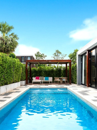 http://Modern%20backyard%20with%20a%20shimmering%20blue%20pool,%20surrounded%20by%20lush%20greenery%20and%20a%20stylish%20seating%20area%20under%20a%20wooden%20pergola.