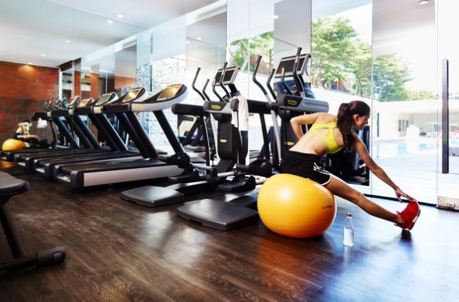 http://A%20woman%20in%20activewear%20stretches%20on%20a%20yellow%20exercise%20ball%20in%20a%20modern%20gym%20with%20a%20row%20of%20treadmills.%20Large%20windows%20reveal%20trees,%20creating%20a%20refreshing%20atmosphere.